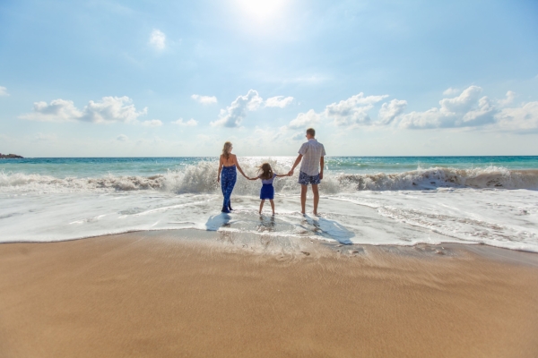 two parents and child holding hands near waves in ocean